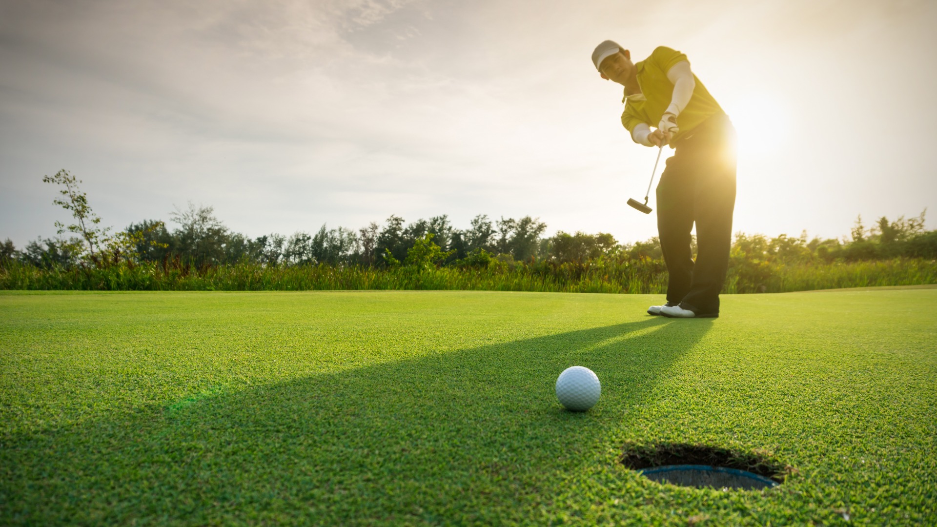 golfer putting ball into hole with sunsetting behind