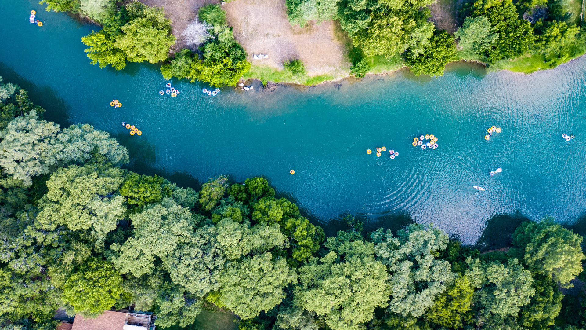 Aeiral image of turquoise water along Comal river with people floating in bright colored tubes