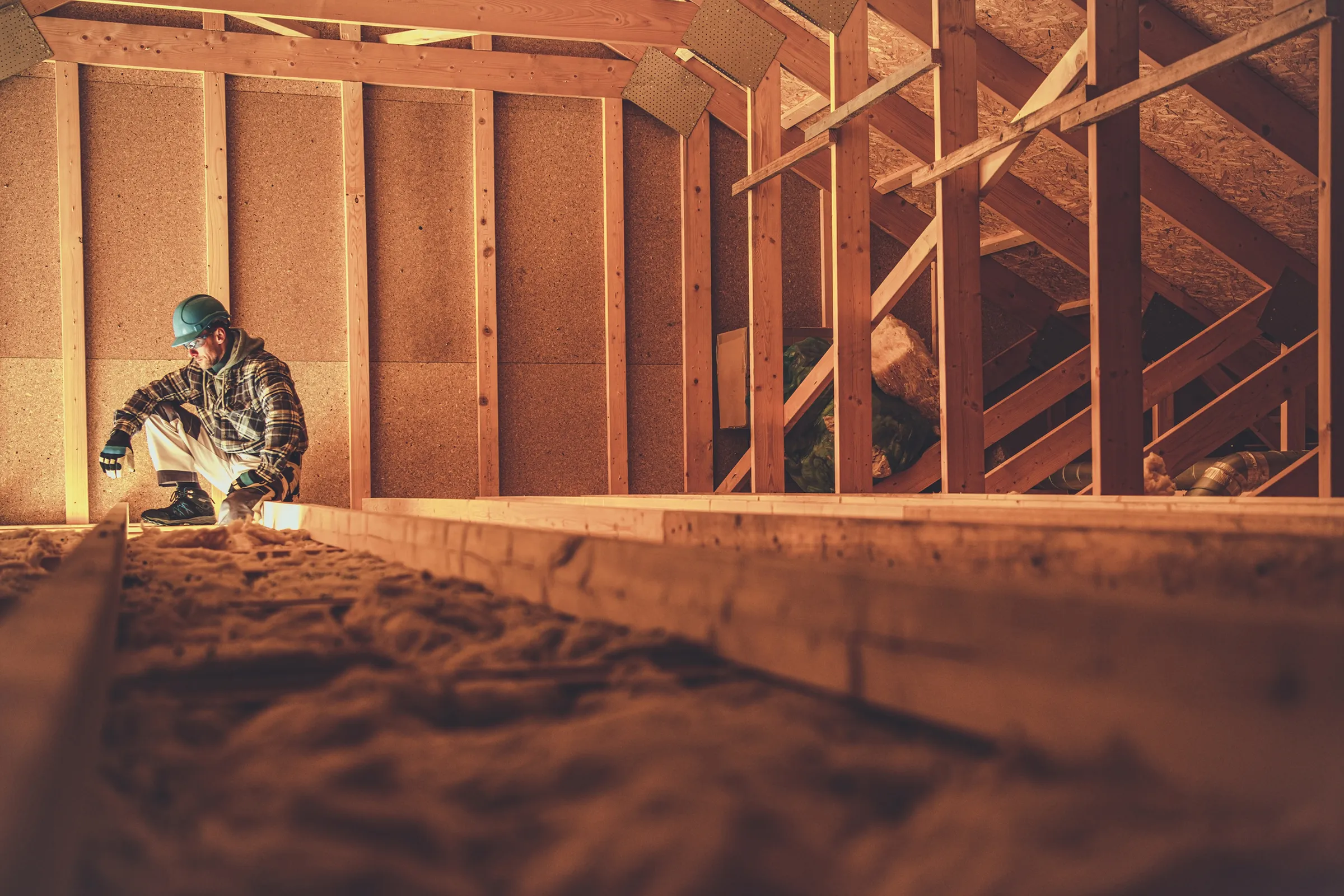 Man wearing hardhat crouched in attic