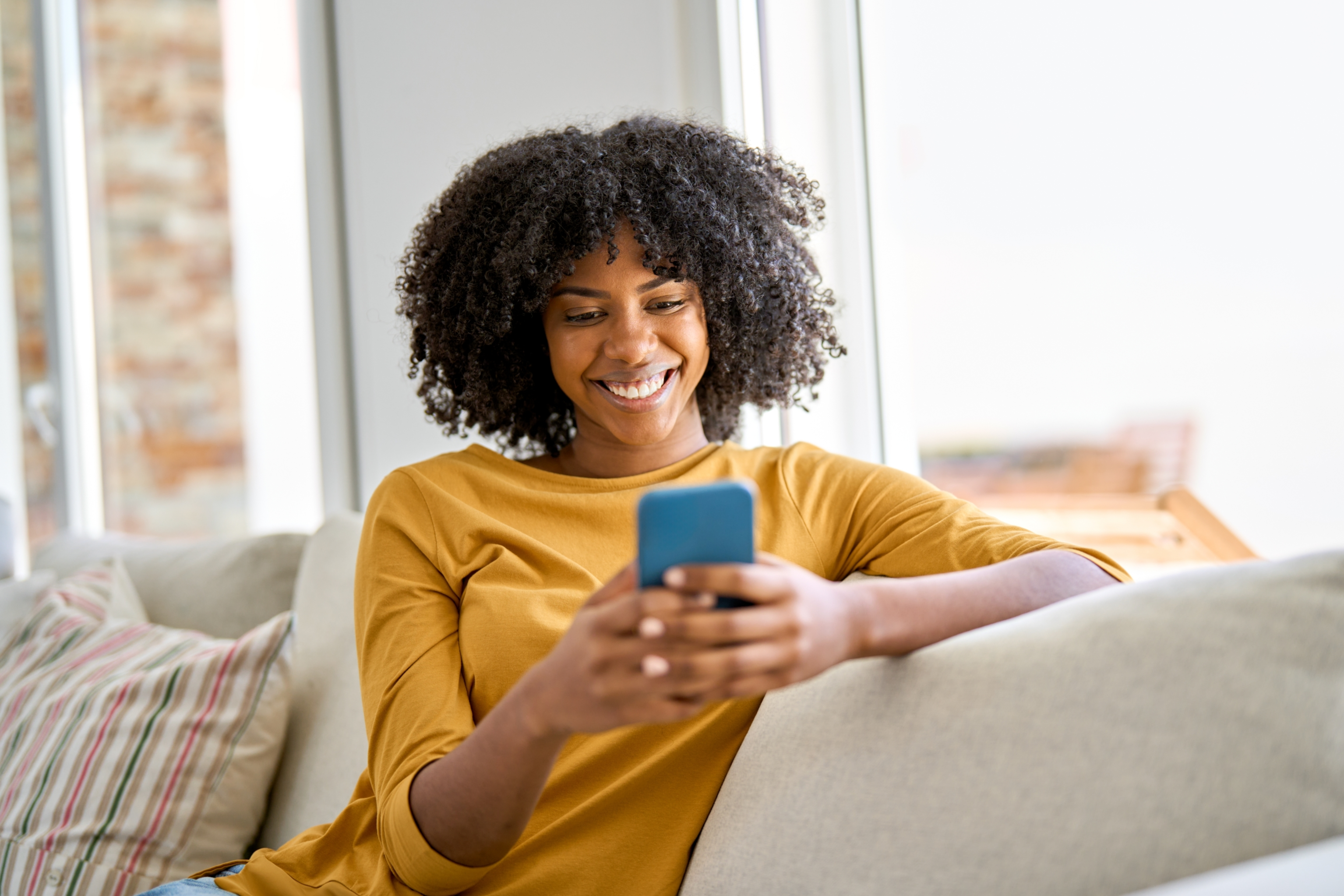 young black woman using phone in apartment and smiling