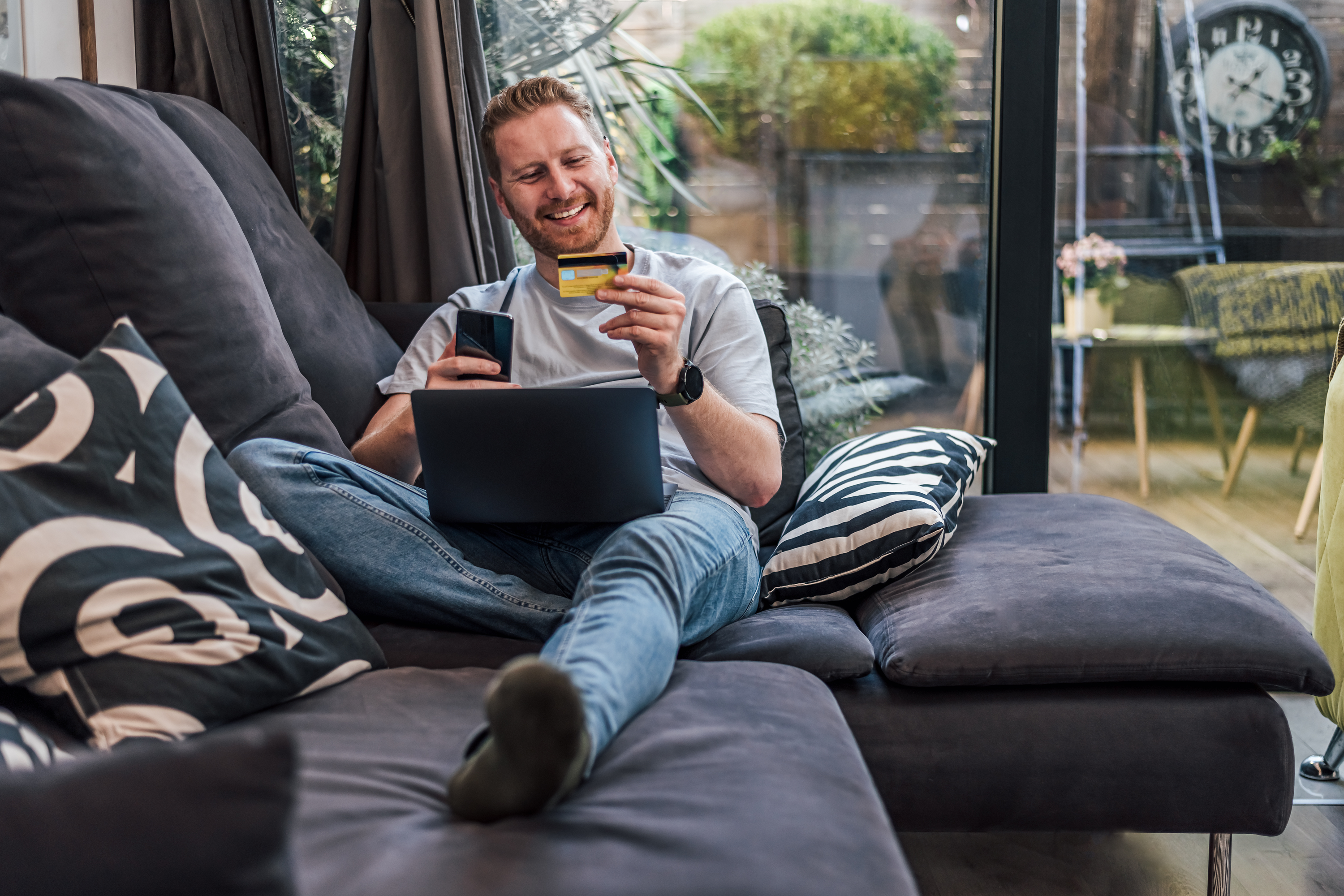 Smiling man on couch looking at credit card